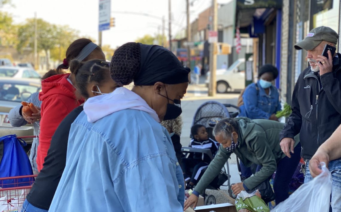 people serving food to people waiting in line to pick up groceries