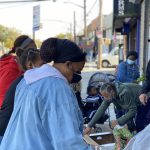 people serving food to people waiting in line to pick up groceries