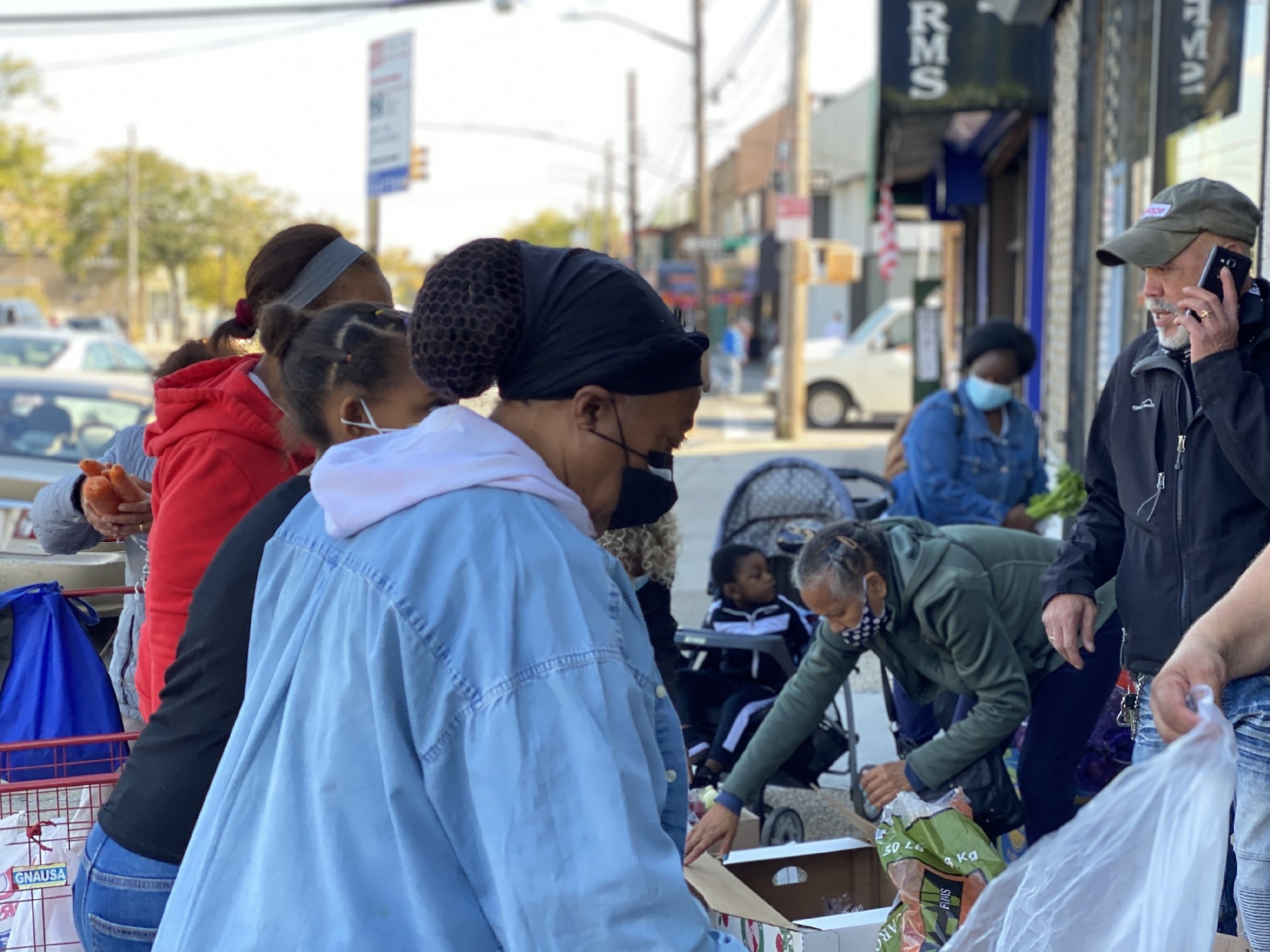 people serving food to people waiting in line to pick up groceries
