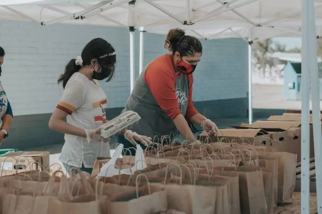man in red shirt getting ready to hand out a bag of food while a young girl puts a dozen eggs into another bag