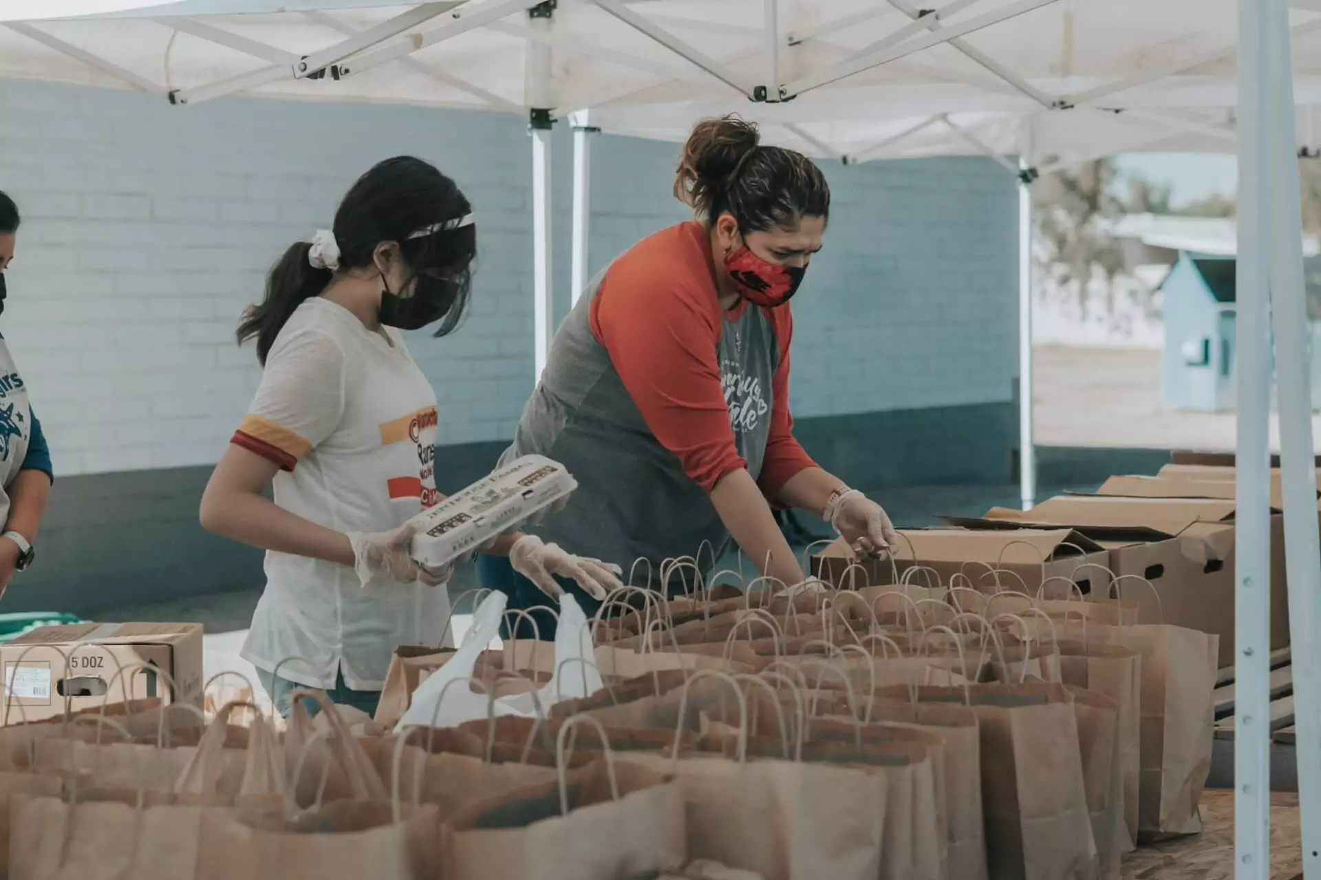 man in red shirt getting ready to hand out a bag of food while a young girl puts a dozen eggs into another bag