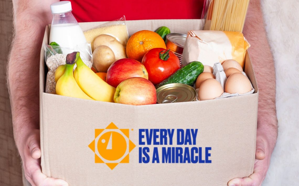 Person holding Every Day is a Miracle box full of groceries to be delivered