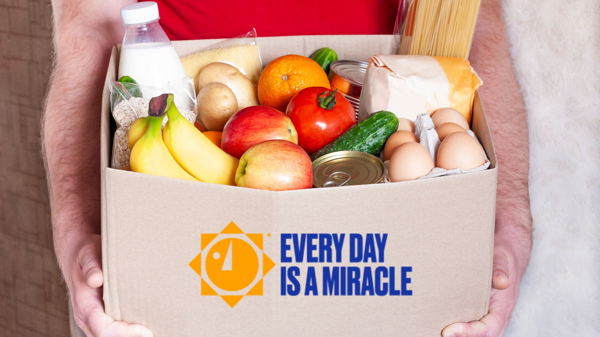 Person holding Every Day is a Miracle box full of groceries to be delivered
